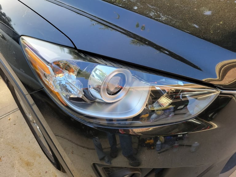 Close-up of a damaged car headlight assembly on a blue vehicle showing cracked lens and exposed internal components
