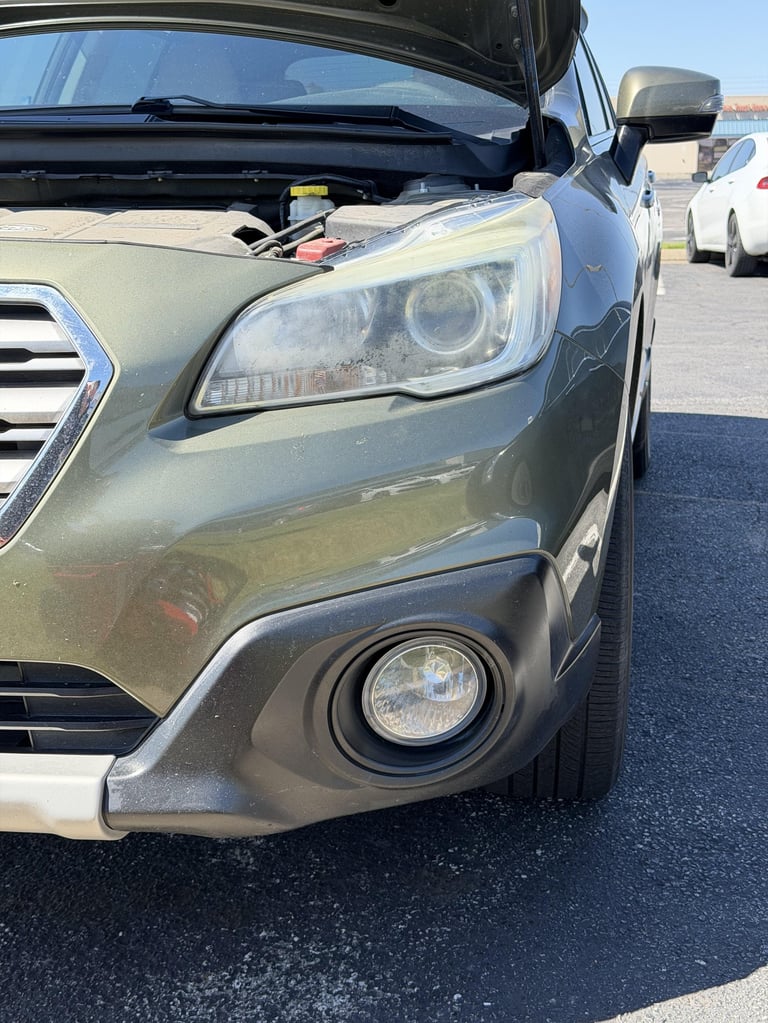 Silver car with open hood in a parking lot showing headlight and fog light details