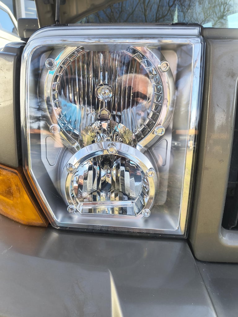 Close-up of a vehicle headlight assembly with dual round lamps and chrome trim, showing internal reflectors and housing