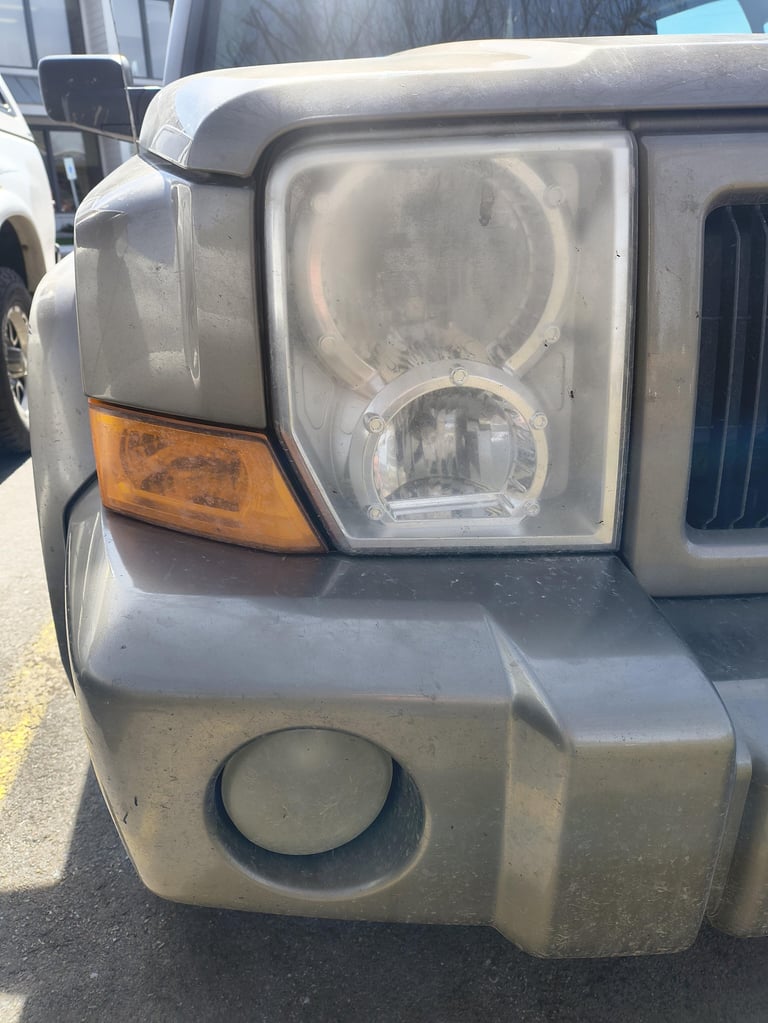 Close-up of a silver SUV front end showing headlight, amber turn signal, and fog light in a parking lot