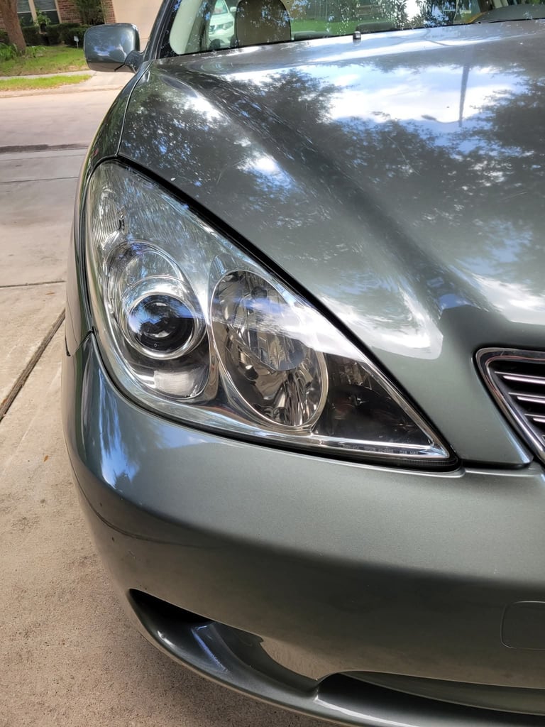 Close-up of a silver sedans front headlight and hood on a driveway
