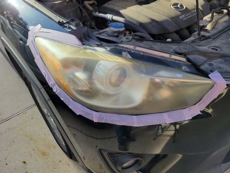Close-up of a cars headlight assembly wrapped in purple tape during repair or restoration work